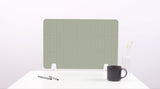 Sage green grid desk divider with white mounting brackets, displayed on white desk with pens, mug, and vase.