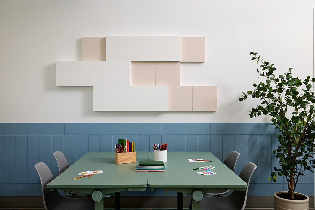 Modern office space with a green table, chairs, and acoustic 3d boxes on the wall above wainscoting