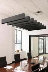 Dark gray felt acoustic beams suspended from ceiling in office conference room above wooden table.