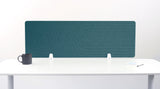 Teal desk divider with geometric line pattern mounted on white desk with support brackets.