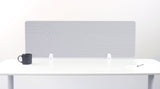 Light gray desk divider with geometric line pattern mounted on white desk with black mug and supplies.