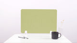 Lime green desk divider with wavy cutout design, positioned upright on white desk with pens, mug, and vase.
