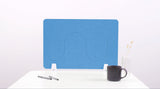 Blue desk divider with wavy cutout design, two white support feet, positioned on white desk with mug and pens.