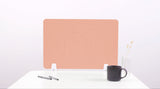 Peach-colored desk divider with wave cutouts, shown standing on white desk with pens, mug, and vase.