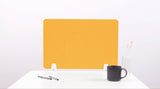 Yellow desk divider with two rounded rectangular cutouts, positioned on white desk with pens, dark mug, and vase.