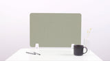 Sage green desk divider with wavy cutout design, positioned on white desk with pens, mug, and vase.