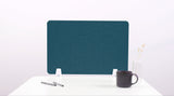 Teal desk divider with rounded arches and white base brackets, displayed on white surface with coffee mug and plants.