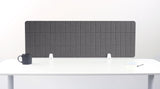 Gray fabric desk divider with vertical grid pattern and white mounting brackets on white desk.