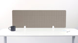 Beige grid-patterned desk divider with white mounting brackets on white desk surface.