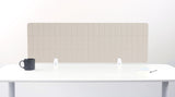 Beige grid desk divider panel with vertical segments mounted on white desk with bracket supports.