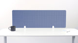 Blue grid-pattern desk divider panel mounted on white desk with black mug and notepad visible.