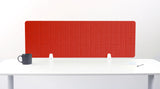 Red grid desk divider with white mounting brackets, positioned on white desk with black mug and notepad.