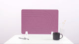 Purple desk divider with curved line pattern and white metal stand on white desk with mug and supplies.