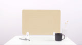 Beige desk divider with curved line pattern, positioned on white desk with pens, dark mug, and vase.