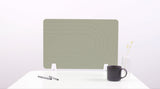 Sage green desk divider with curved line pattern, mounted on white desk with pens, mug, and vase.