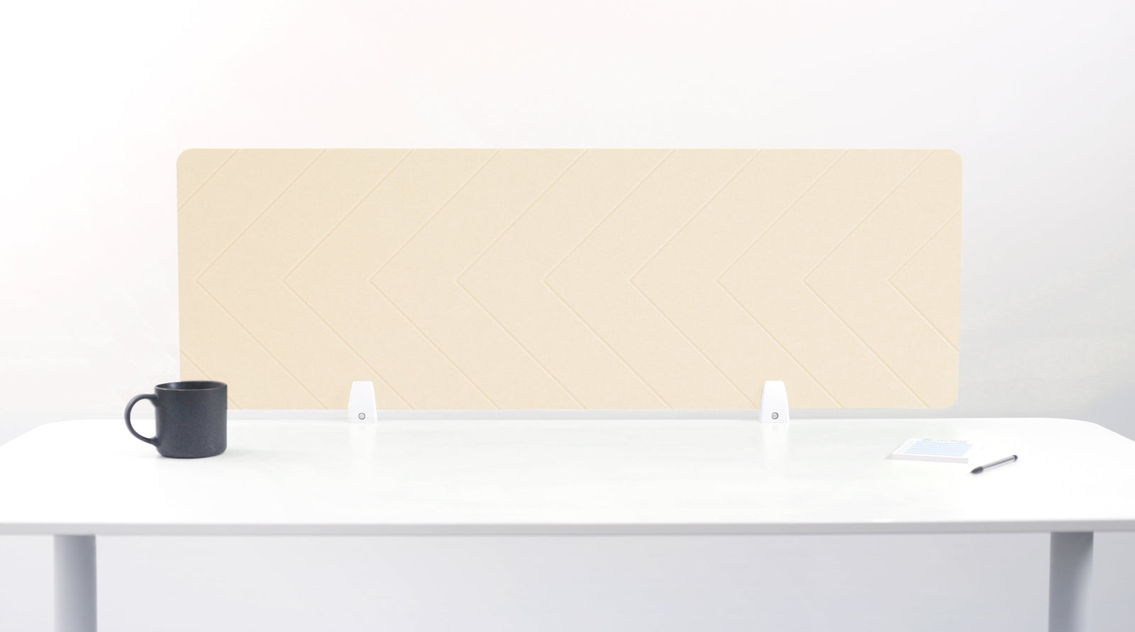 An ivory-colored felt desk divider placed on a white desk with a black mug and a pen beside it.