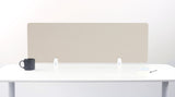 Beige desk divider with chevron pattern mounted on white desk with metal brackets, dark mug and notepad visible.