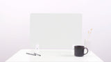 Light gray desk divider with geometric pattern positioned on white desk beside pens, dark mug, and vase with dried flowers.