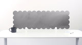 Gray scalloped headboard against a white wall with a white desk and black mug.