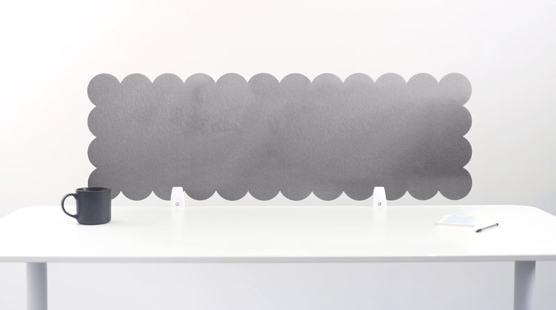 Gray scalloped headboard against a white wall with a white desk and black mug.