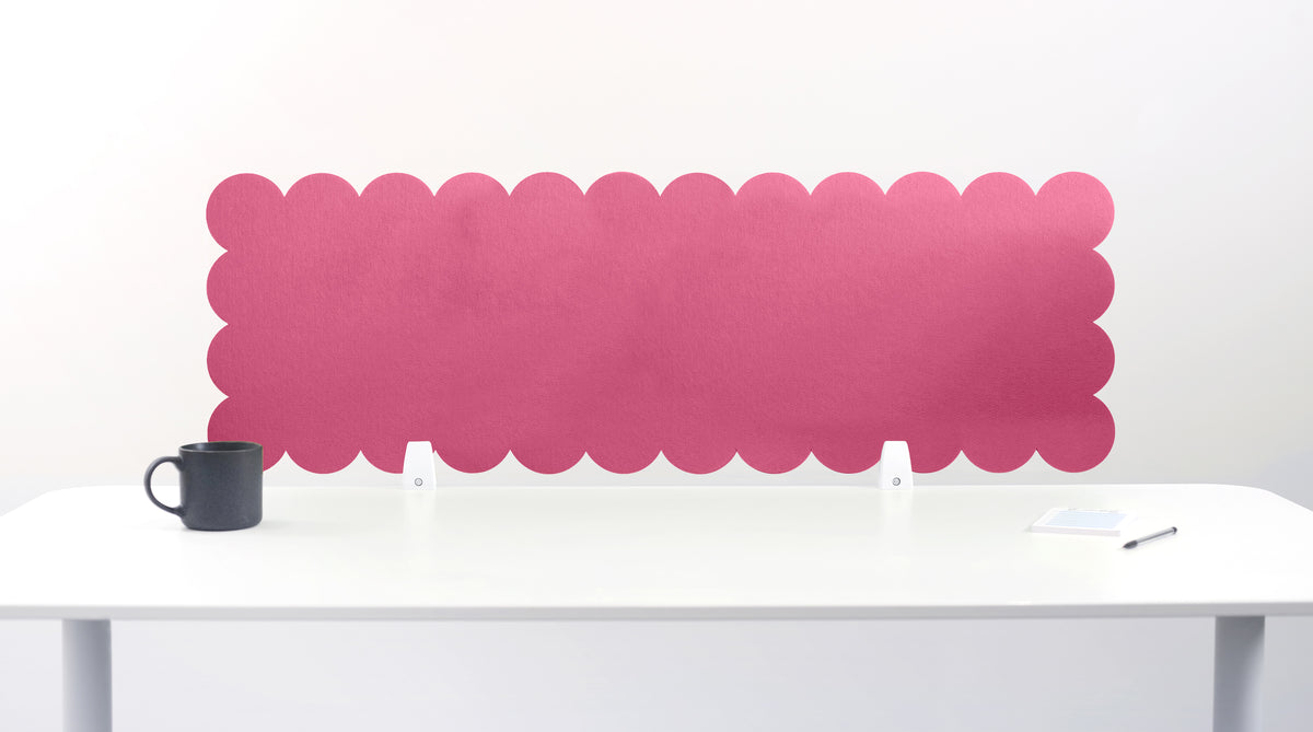 Pink scalloped headboard against a white wall with a white desk and black mug.