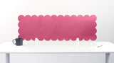 Pink scalloped headboard against a white wall with a white desk and black mug.