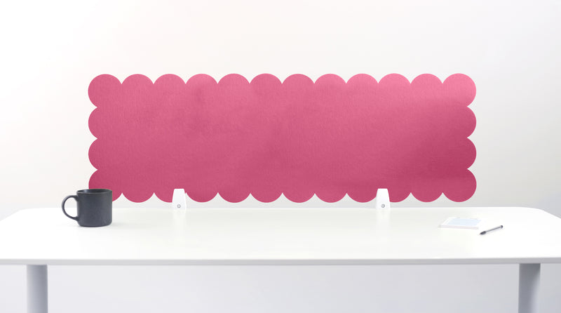 Pink scalloped headboard against a white wall with a white desk and black mug.