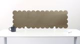 Scalloped headboard attached to a white wall above a white table with a black mug on it.