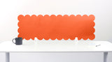 Orange scalloped headboard against a white wall with a white desk and black mug.