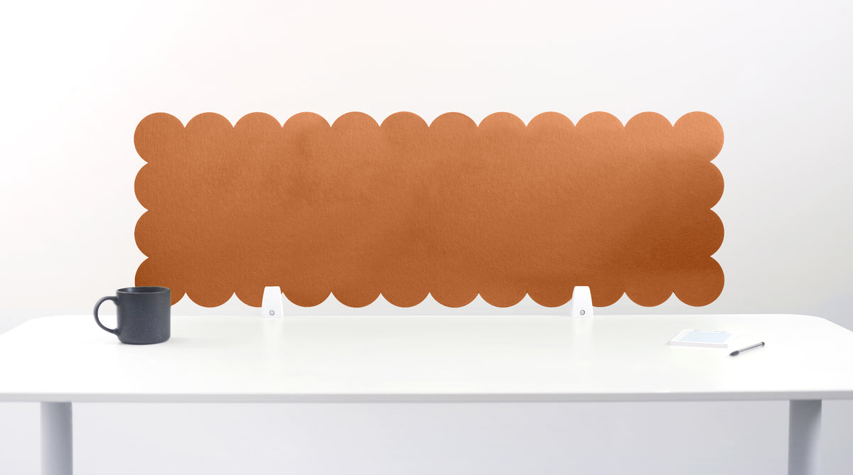 Brown scalloped headboard on a white wall above a white desk with a black mug.