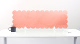 Pink scalloped headboard on a white wall above a white table with a black mug.