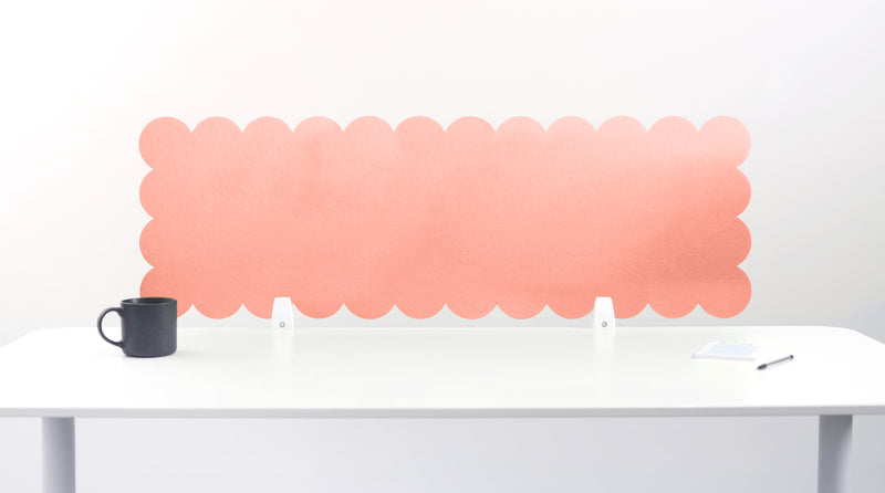 Pink scalloped headboard on a white wall above a white table with a black mug.