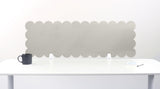 White scalloped headboard on a white wall with a white table and black mug in front.