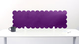 Purple scalloped headboard on a white wall above a white desk with a black mug.