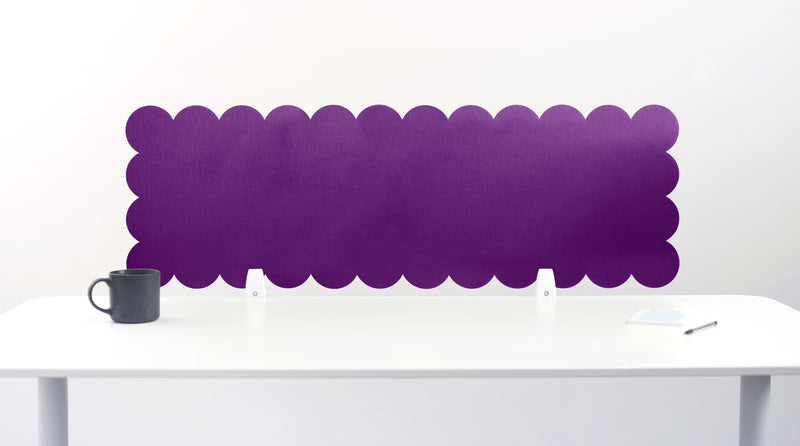 Purple scalloped headboard on a white wall above a white desk with a black mug.