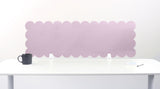 Pink scalloped headboard on a white wall with a white table and black mug in the foreground.