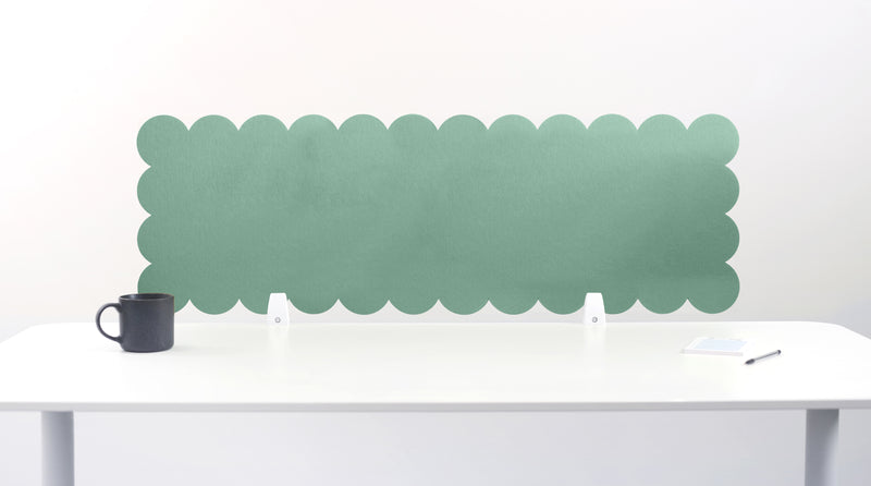 Green scalloped headboard against a white wall with a white desk and black mug.