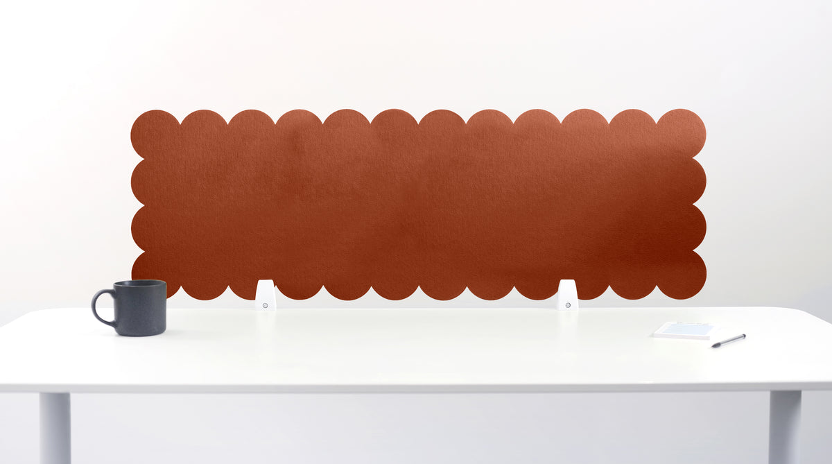 Brown scalloped headboard on a white wall above a white desk with a black mug.