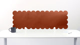 Brown scalloped headboard on a white wall above a white desk with a black mug.