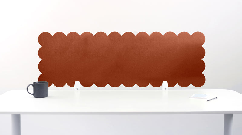 Brown scalloped headboard on a white wall above a white desk with a black mug.