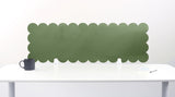 Green scalloped headboard against a white wall with a white table and black mug.