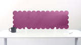 Purple scalloped headboard against a white wall with a white desk and black mug.