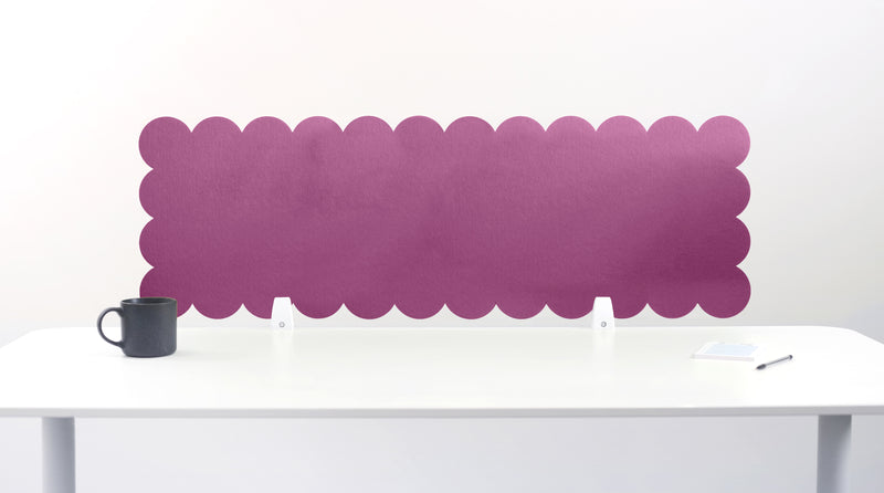 Purple scalloped headboard against a white wall with a white desk and black mug.