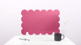 Pink scalloped screen on a white surface with a black mug and pen.