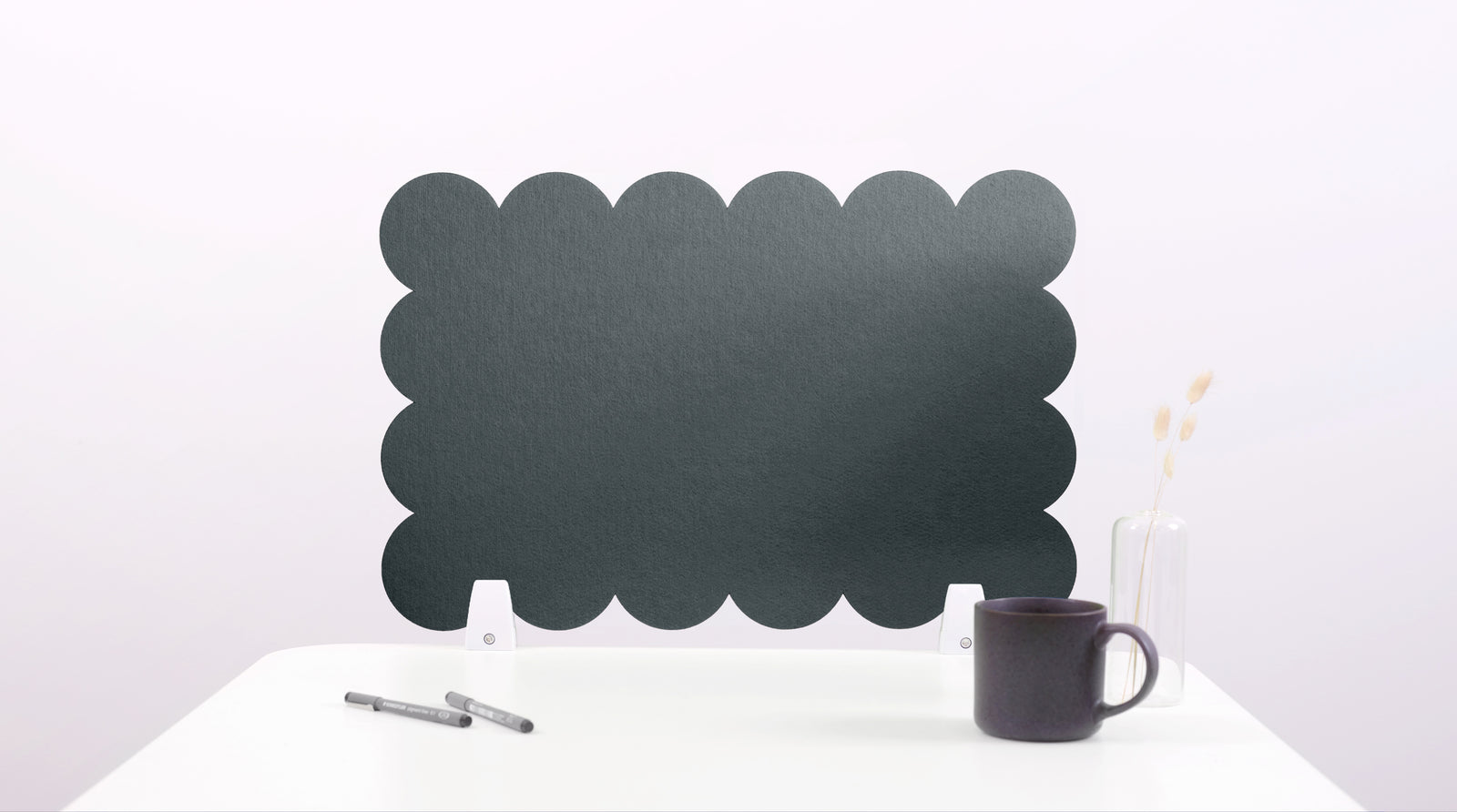 Green scalloped screen on a white surface with a black mug and pen.