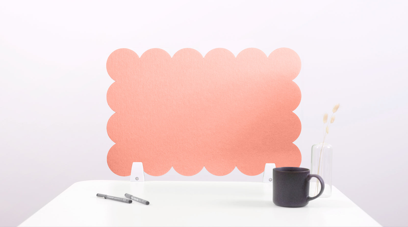 Pink cloud-shaped screen on a white surface with a black mug and pen.