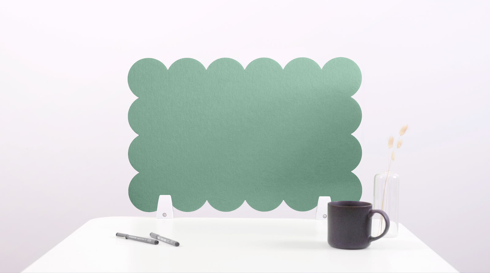 Green scalloped headboard on a white background with a black mug and pen.