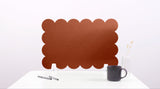 Brown scalloped placemat on a white surface with a mug and pen.