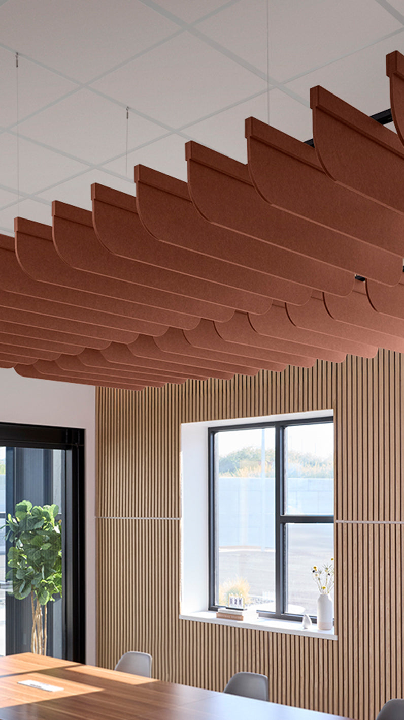 Reddish-brown acoustic ceiling blade baffles suspended from the ceiling, installed in a conference room. Felt Right's acoustic blade baffles absorb 65% of sound waves, making office spaces quieter and feel more calm.