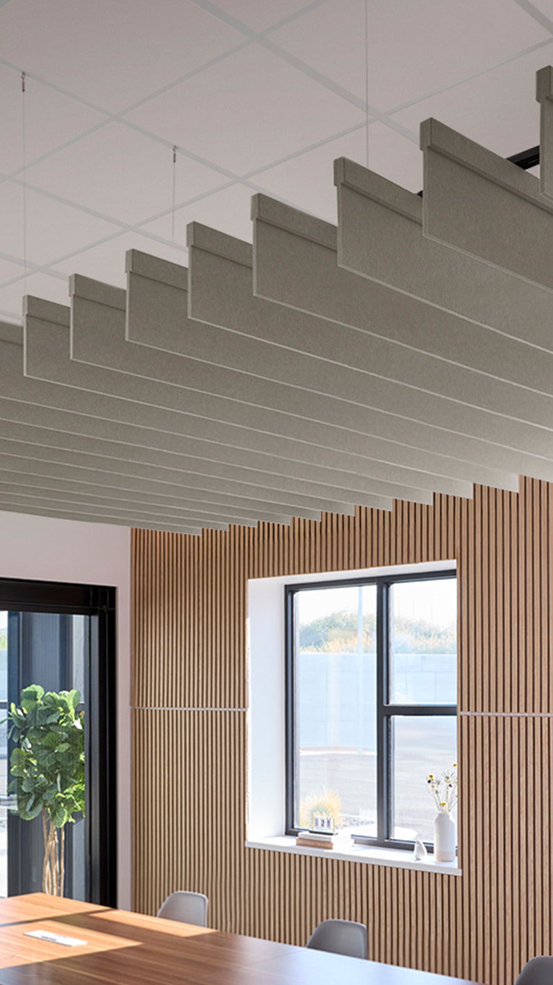 Light brownish-grey acoustic ceiling blade baffles suspended from the ceiling, installed in a conference room. Felt Right's acoustic blade baffles absorb 65% of sound waves, making office spaces quieter and feel more calm.